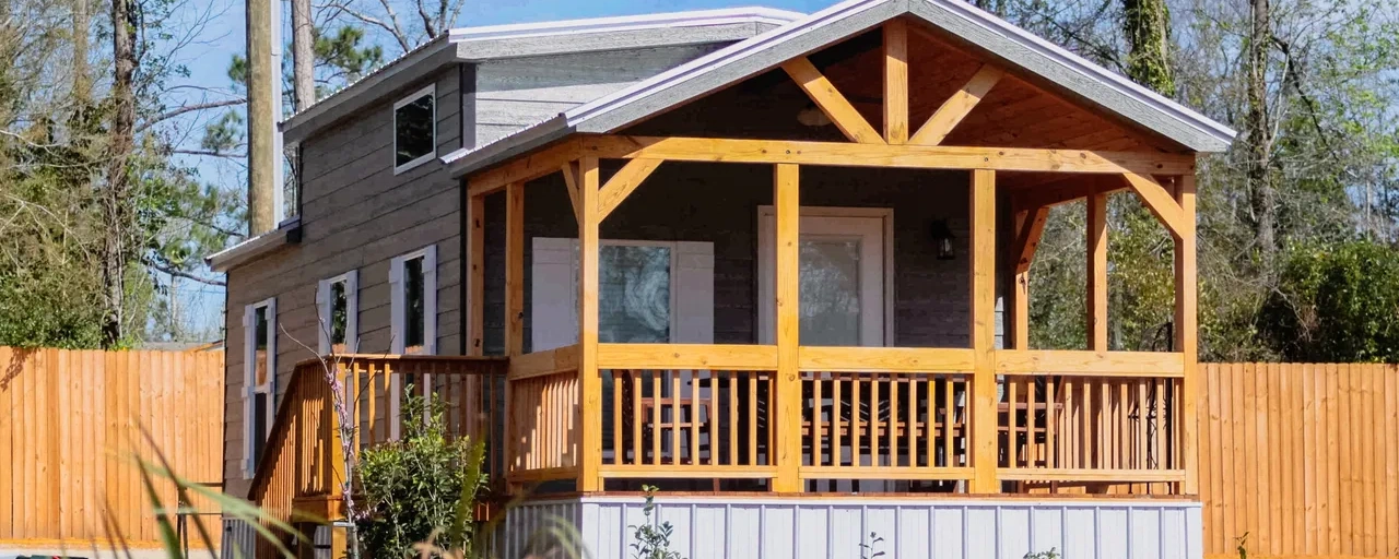 A gray-sided cabin with a timber-framed covered porch and railed steps.