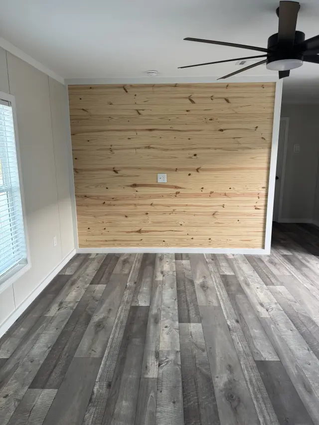 Living room accent wall of natural knotty pine planks above gray plank flooring, with a ceiling fan overhead.