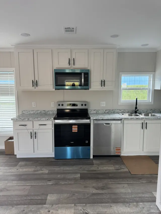 Kitchen with white shaker cabinets, a stainless steel range, microwave and dishwasher, speckled countertops and a window over the sink.