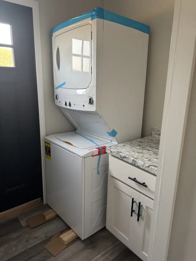 Stacked washer and dryer in a laundry nook next to a white cabinet and a dark front door.