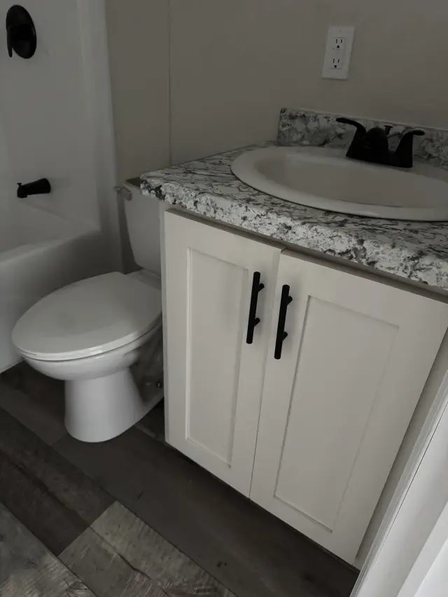 Bathroom with a white vanity with black pulls, a speckled countertop, toilet and tub with black fixtures.
